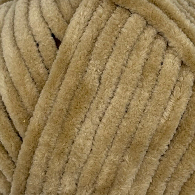 A close-up of thick, plush velvet yarn in a warm tan or light brown color, showing the ribbed texture and soft fibers.