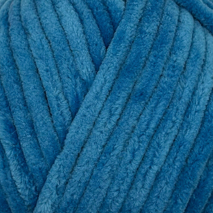 A close-up of thick, plush corded yarn in a medium blue color, showing the soft, fuzzy texture of the fibers.