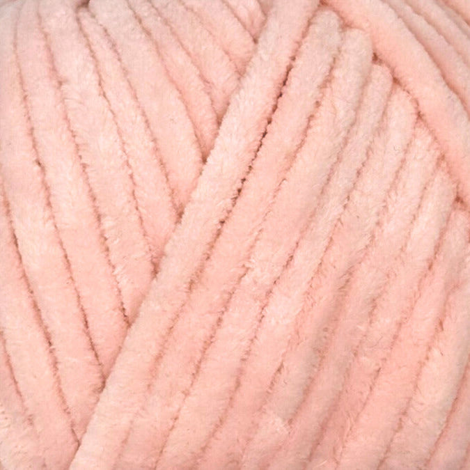 A close-up of thick, soft yarn in a light pastel pink color, showing the fuzzy texture of the strands.