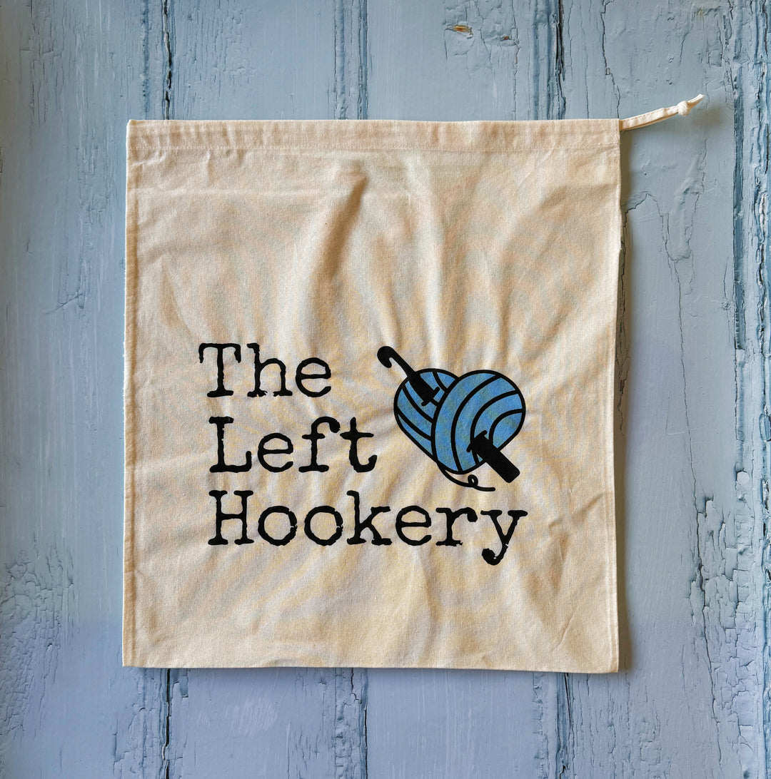 Beige drawstring bag with 'The Left Hookery' text and logo on a textured blue background