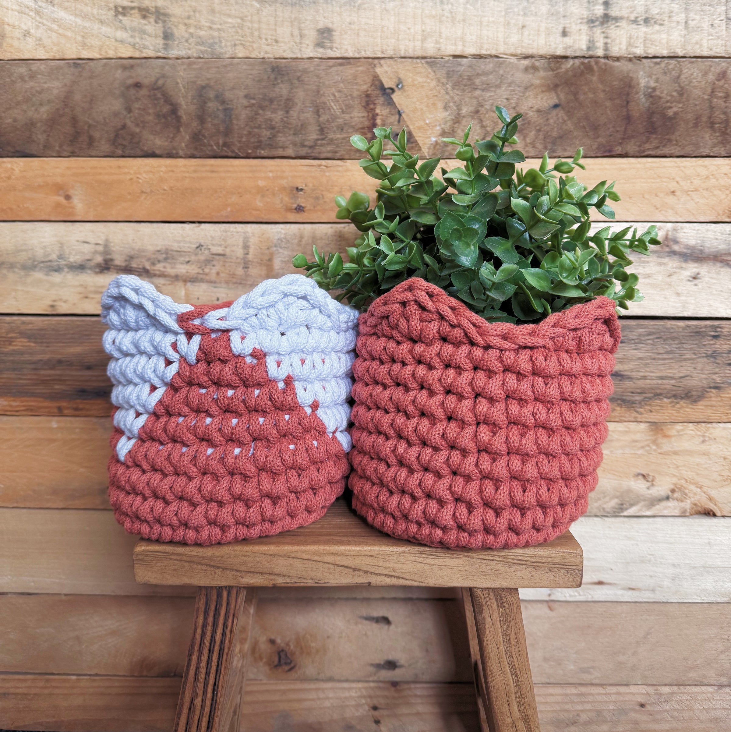 Two crocheted planters with a plant on a wooden stool against a wooden wall.