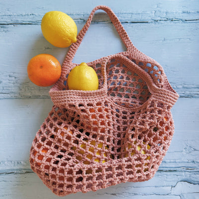 Pink crochet bag with fruits on a light blue wooden surface