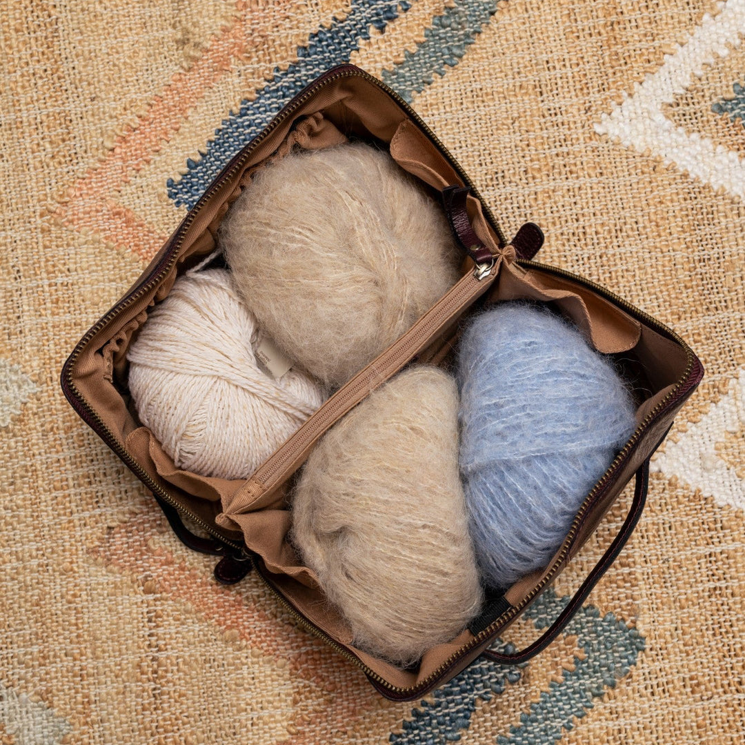 Three balls of yarn in a yarn bag on a textured fabric background