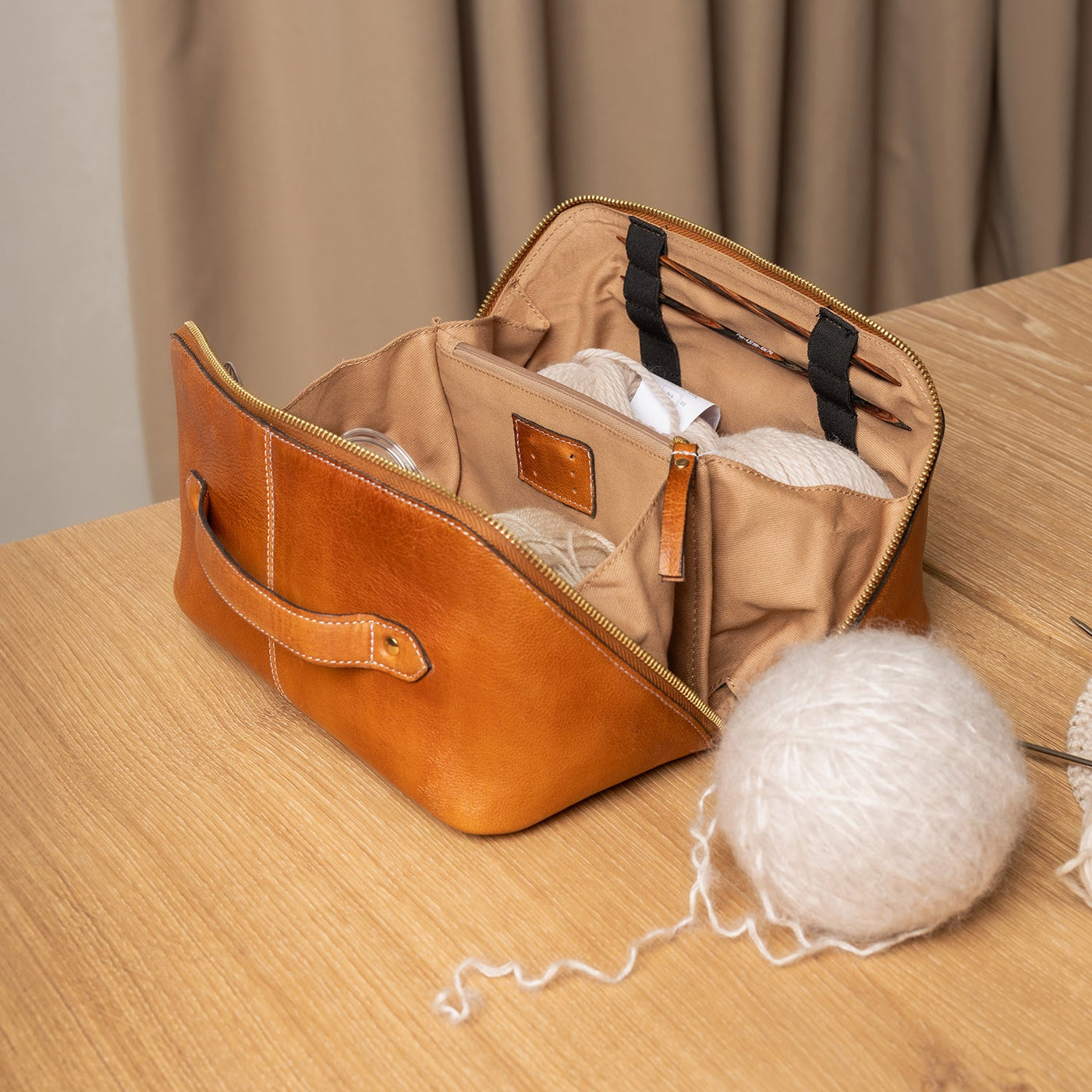 Brown leather bag with a beige interior on a wooden surface with a beige curtain in the background