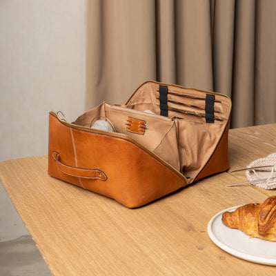 Brown leather bag on a wooden table with a plate of food and a curtain in the background