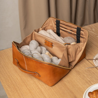 Brown leather bag with yarn inside on a wooden surface