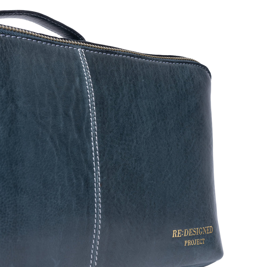 Close-up of a dark blue textured leather bag corner with white contrast stitching and gold &
