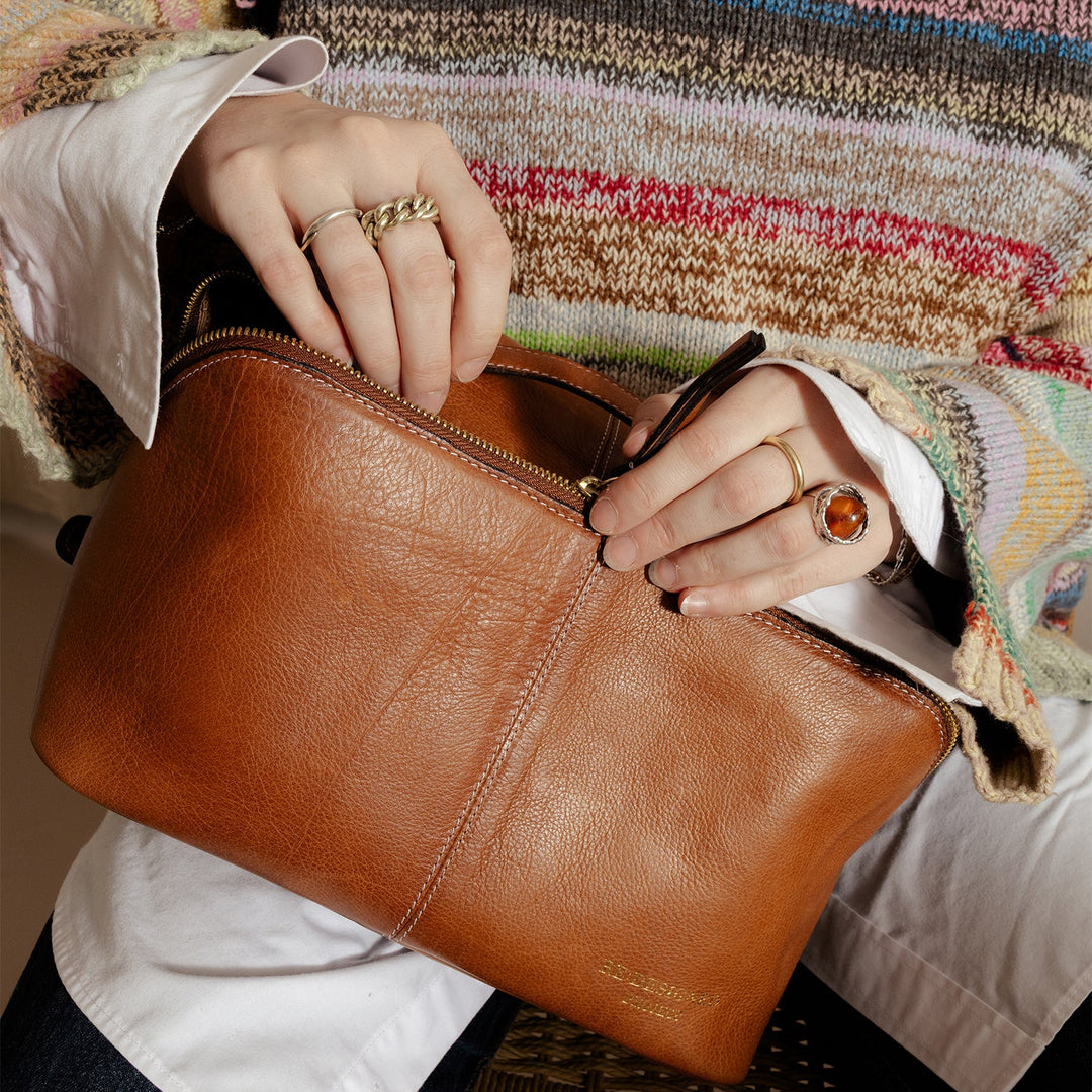 Person holding a brown leather clutch with a colorful striped sweater in the background