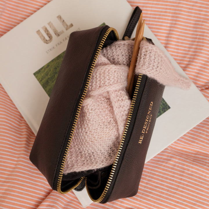 Brown leather pouch with pink knitted item on a magazine with &