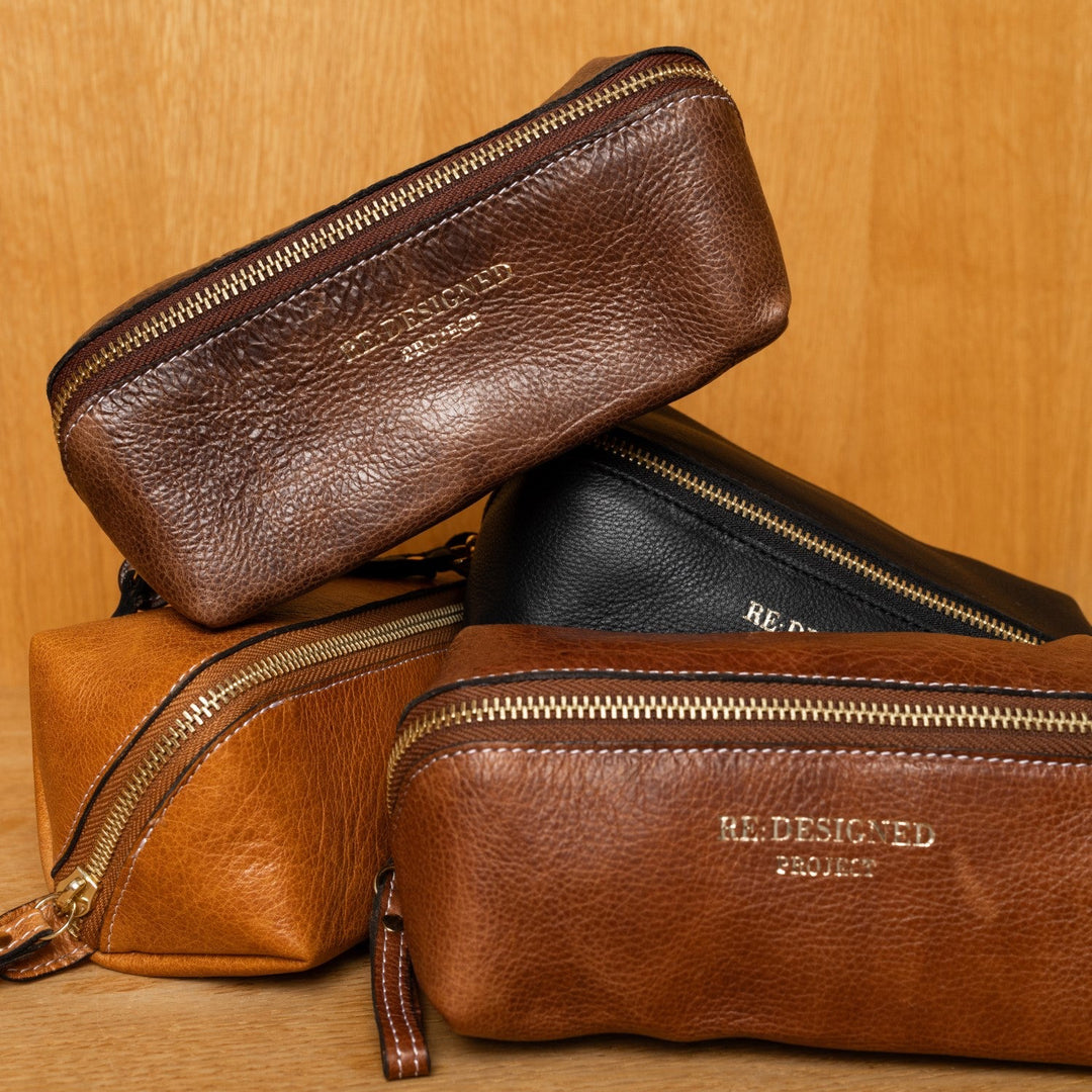 Four leather pouches in brown and black with gold zippers on a wooden surface.