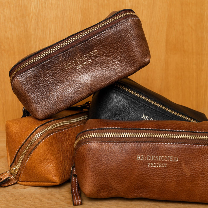 Four leather pouches in brown and black with gold zippers on a wooden surface.