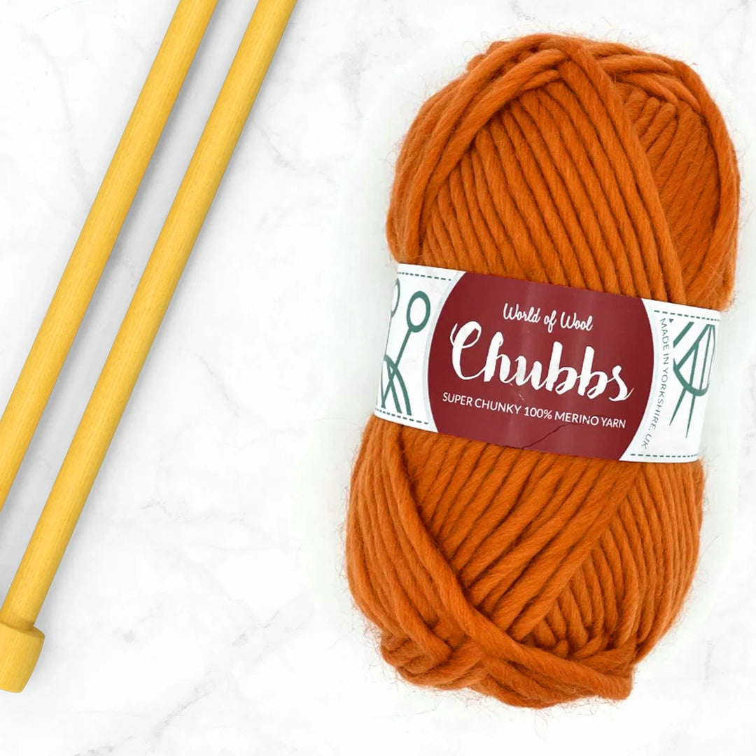 ball of orange super chunky yarn with knitting needles beside it