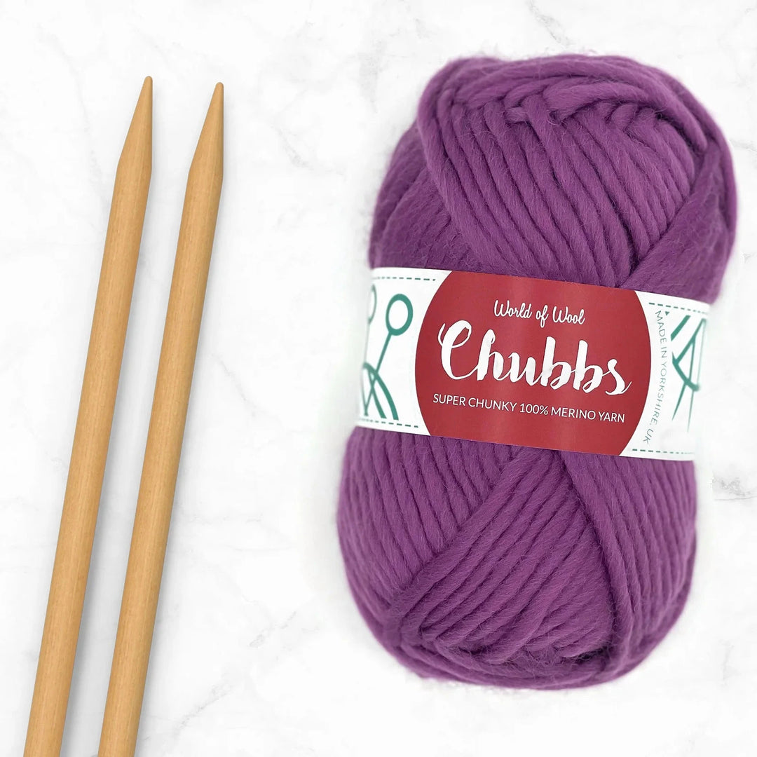 purple ball of super chunky yarn next to some bamboo knitting needles