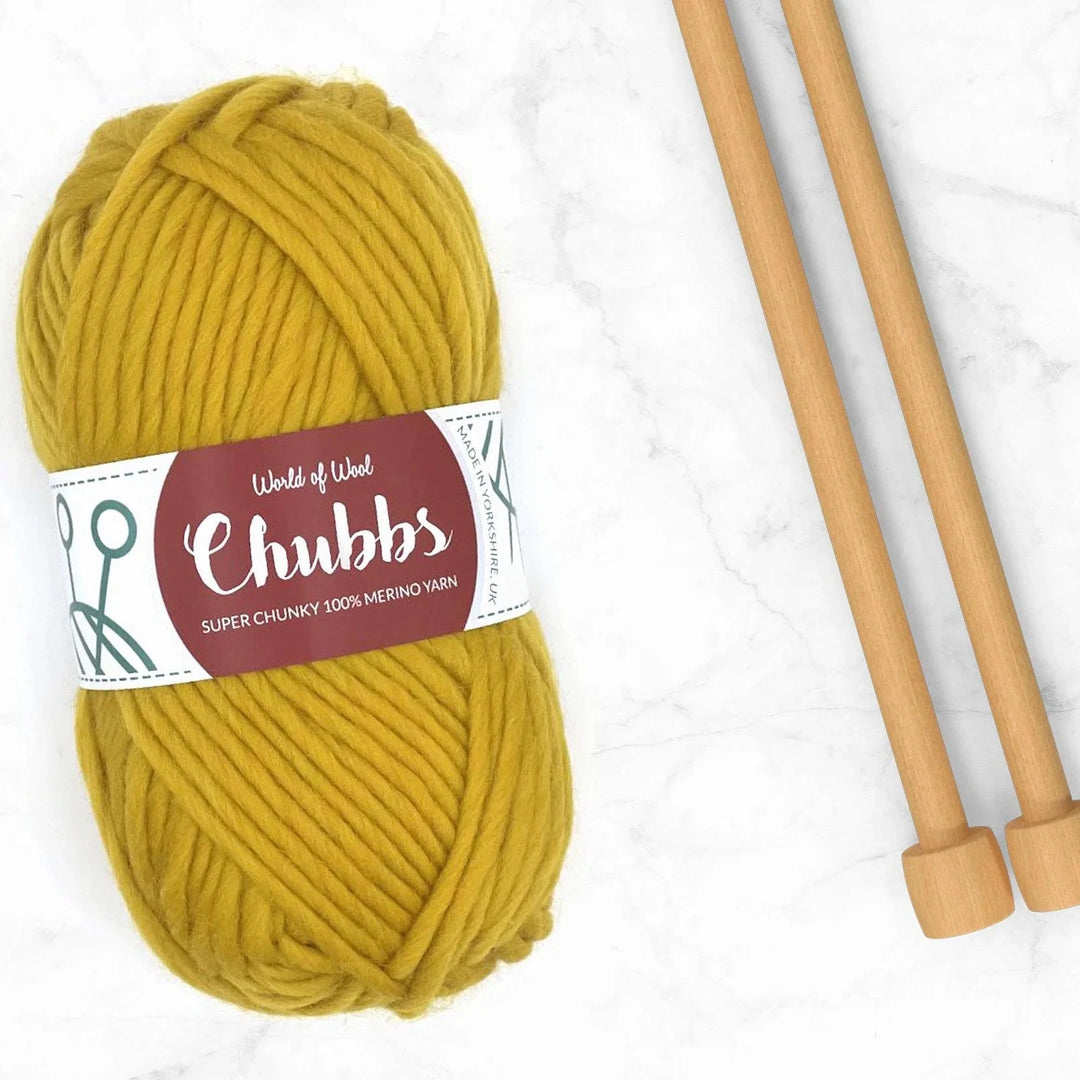 ball of mustard yarn next to bamboo knitting needles on a marble background