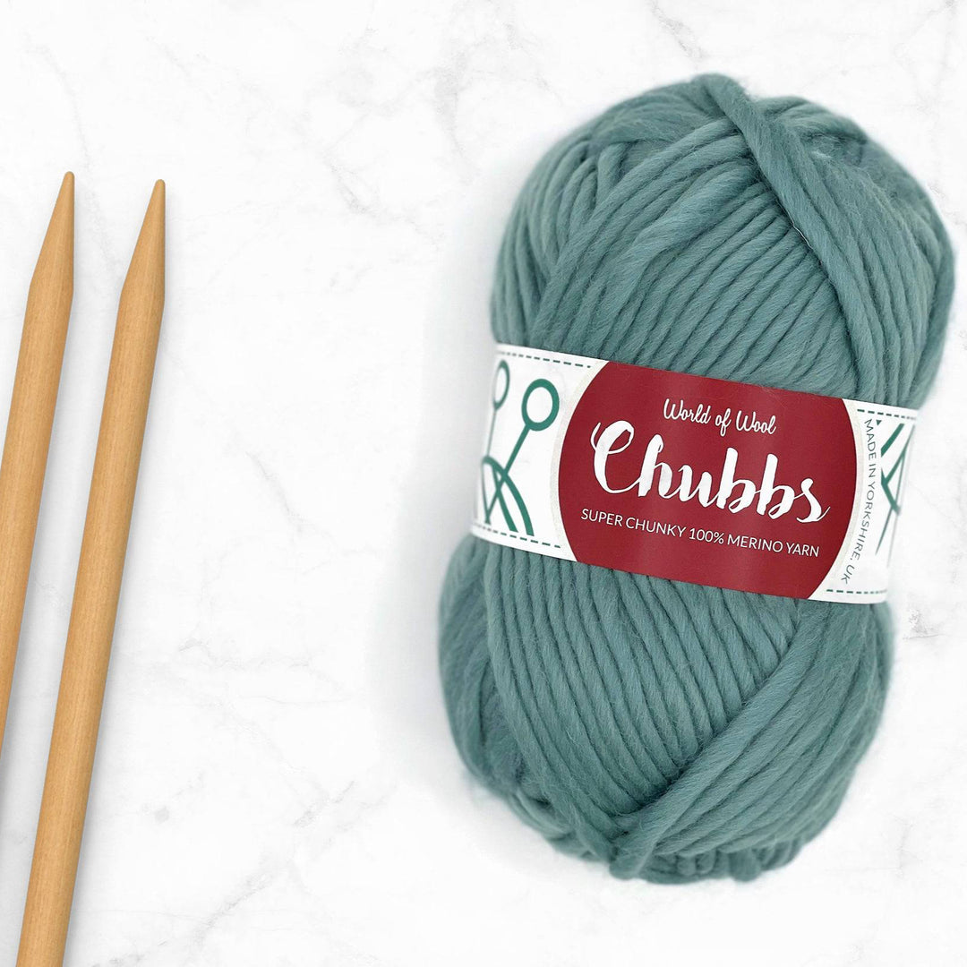 teal yarn ball on a marble backhground next to some bamboo knitting needles